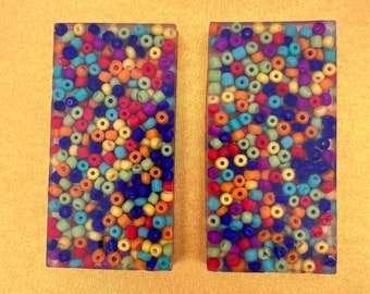 May include: Two rectangular clear resin blocks filled with colorful beads. The beads are in various shades of blue, green, yellow, orange, red, and purple.