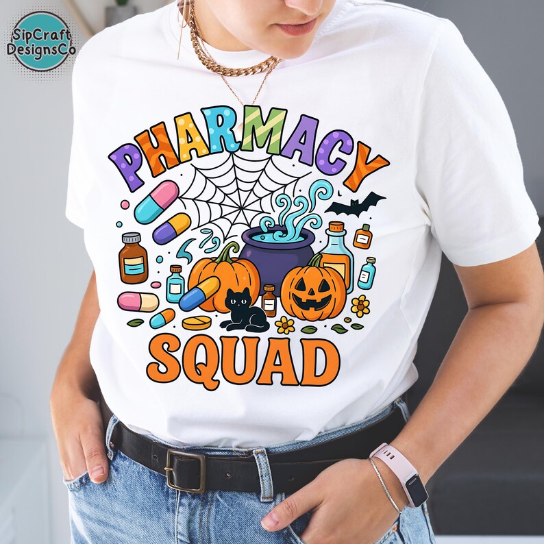 May include: White t-shirt with a colorful "PHARMACY SQUAD" graphic. The design includes pumpkins, pills, a black cat, a cauldron, and a spiderweb, all in a Halloween theme. The shirt has a crew neck and short sleeves.