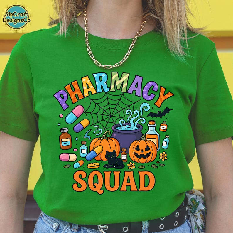 May include: Green t-shirt with a colorful "PHARMACY SQUAD" graphic. The design includes pumpkins, pills, a black cat, and a spiderweb, perfect for Halloween. The shirt has short sleeves and a crew neck.