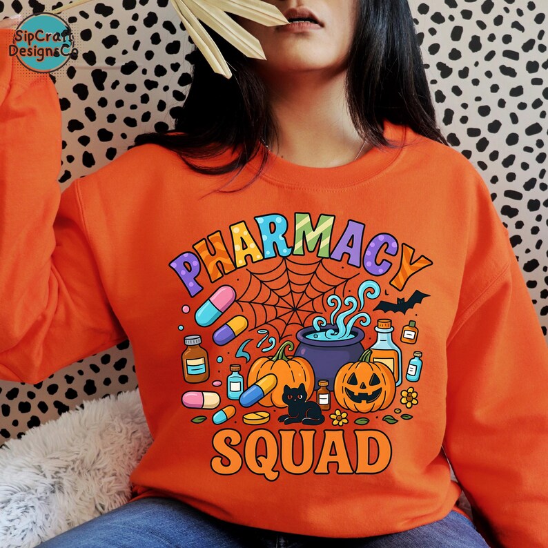 May include: Orange sweatshirt with a colorful "PHARMACY SQUAD" graphic. The design includes pills, pumpkins, a black cat, a cauldron, and a spider web, perfect for Halloween. The sweatshirt is a crew neck.
