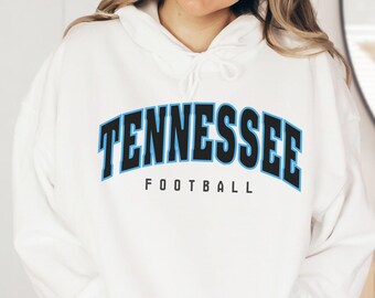 May include: White hoodie with the word "TENNESSEE" in black and light blue block letters, with "FOOTBALL" in black below. The hoodie has a drawstring and a front pocket.
