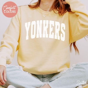 May include: A yellow sweatshirt with the word "YONKERS" printed in white on the front.