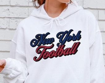 May include: White hoodie with a front pocket and drawstring. The text "New York Football" is displayed in blue and red script. The hoodie is a casual garment.
