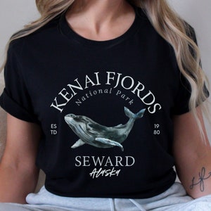 May include: Black t-shirt with a white graphic design featuring a whale and the text "Kenai Fjords National Park" and "Seward Alaska".