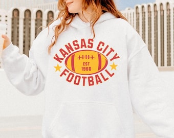 Peut inclure: Sweat-shirt blanc avec un graphique rouge et jaune d'un ballon de football avec le texte "Kansas City Football Est 1960".