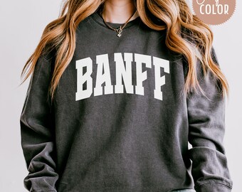May include: A dark gray sweatshirt with the word "BANFF" printed in white on the front. The sweatshirt has a relaxed fit and long sleeves.