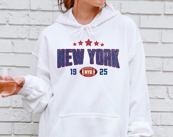 May include: White hoodie with a front graphic. The graphic features the text "NEW YORK" in blue and red, with red stars above and the numbers "19" and "25" flanking a football with "NYG" in the center. The hoodie has a drawstring.
