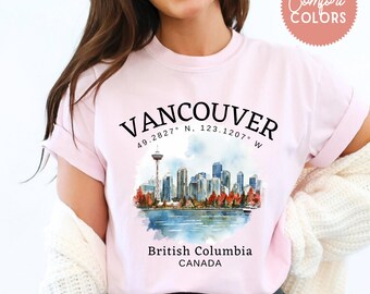 May include: Light pink t-shirt with a Vancouver, British Columbia, Canada graphic. The design features the city skyline, the Space Needle, and the text "Vancouver" above the coordinates 49.2827° N, 123.1207° W.
