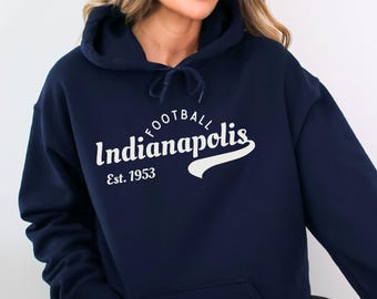May include: Navy blue hooded sweatshirt featuring the text "Indianapolis Football Est. 1953" in white script. The sweatshirt has a drawstring hood and a front pocket. The theme is sports apparel.