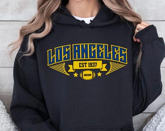 May include: A navy blue hoodie with the text "LOS ANGELES" in a blue and yellow design. The hoodie also features the text "EST 1937" and a football graphic.
