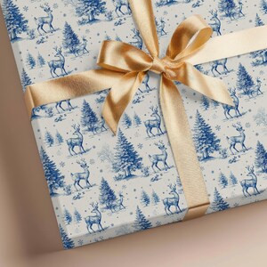 May include: A wrapped gift with a gold satin ribbon. The wrapping paper features a blue and white toile pattern of deer, trees, and snowflakes. The bow is centered on the top of the gift.