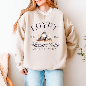 May include: A beige sweatshirt with the text "EGYPT Vacation Club EST. 2025 NORTHEAST AFRICA" and a watercolor illustration of pyramids.