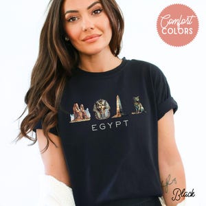 May include: A black t-shirt with a graphic of Egyptian landmarks, including the Sphinx, pyramids, and a tall obelisk. The text "EGYPT" is printed below the graphic.