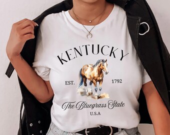 May include: White t-shirt with a brown and white horse illustration. The text "Kentucky Est. 1792 The Bluegrass State U.S.A." is printed on the shirt.