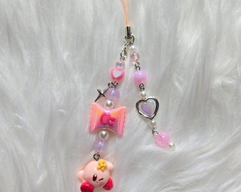 May include: Pink and white phone charm with a pink and white candy charm, a pink heart charm, a pink and white star charm, a pink and white pearl charm, and a pink Kirby character charm.