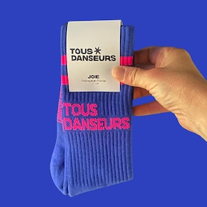 Peut inclure: Chaussettes bleues avec des rayures roses et le texte "TOUS DANSEURS" en rose. Les chaussettes ont une étiquette blanche qui dit "TOUS DANSEURS" et "JOIE Fabriqué en France".