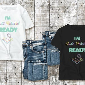 Puede incluir: Dos camisetas con el texto "I'm Audit Rebuttal Ready" en colores arcoíris. Las camisetas están sobre un fondo de madera con pantalones vaqueros azules.
