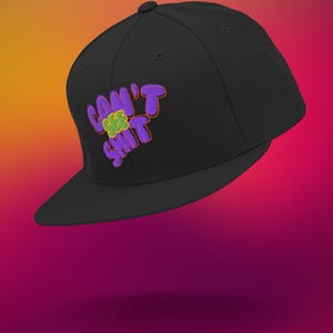 Op de afbeelding: Een zwarte, getailleerde baseballpet met een geborduurd ontwerp in paars en groen met de tekst "Can't See Shit".