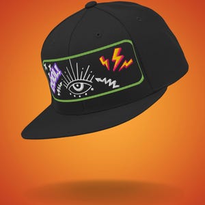Op de afbeelding: Een zwarte baseballpet met een groene, witte, paarse en oranje geborduurde patch met een oog, bliksemschichten en het woord "Cool!"