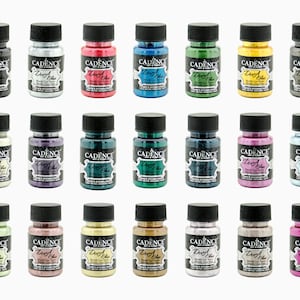May include: Twenty-four bottles of metallic paint in various colors, including silver, gold, red, blue, green, purple, and pink. Each bottle has a black cap and a label that reads "Cadence Dry Rub Metallic Craft Enamel".