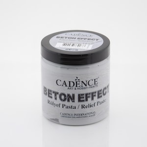 Puede incluir: Un tarro blanco de pasta de relieve Beton Effect de Cadence. El tarro tiene una tapa negra y una etiqueta con el texto "Cadence Art & Hobby Paints Beton Effect Rölyef Pasta / Relief Paste" y "Cadence International London-New York Paris Istanbul Moscow".