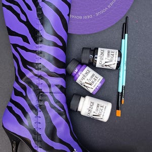 May include: A purple and black zebra print boot with a high heel. Three bottles of leather paint are shown in the image. The bottles are labelled "Cadence Leather Vogue" and are in the colours white, purple, and black.