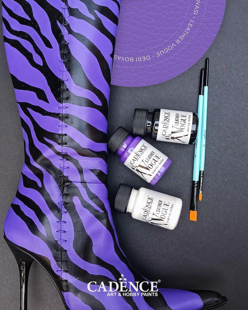 May include: A purple and black zebra print boot with a high heel. Three bottles of leather paint are shown in the image. The bottles are labelled "Cadence Leather Vogue" and are in the colours white, purple, and black.