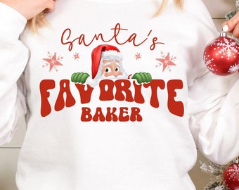 Könnte beinhalten: Weißer Pullover mit einer roten und weißen Grafik von Weihnachtsmann, der über dem Text "Santas Lieblingsbäcker" lugt.