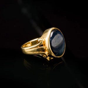 Op de afbeelding: Een gouden ring met een grote, ovale blauwe edelsteen. De ring heeft een eenvoudig, elegant ontwerp.