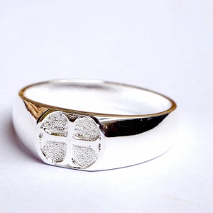 Könnte beinhalten: Ein silberner Ring mit einem Kreuzdesign. Das Kreuz ist erhaben und hat eine strukturierte Oberfläche.