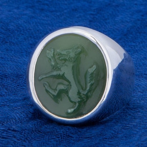 May include: A silver ring with a green stone featuring a carved image of a fox.