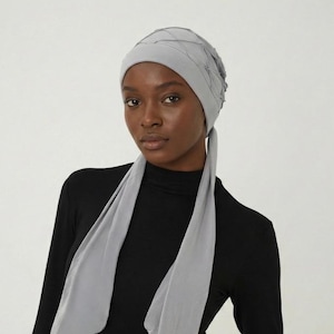 May include: A light gray head covering with a textured design, paired with a matching scarf. The head covering is worn with a black long-sleeve top.