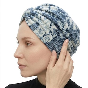 May include: A blue and white patterned turban-style head covering. The fabric has a textured appearance. The person in the image is wearing a black top and a gold bracelet. The head covering is a stylish accessory.