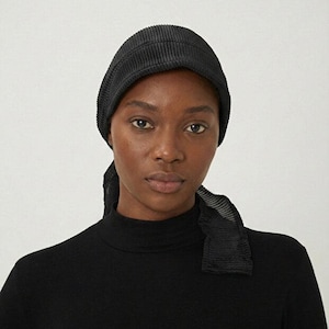 May include: A black ribbed knit beanie and matching scarf are featured in this image. The beanie is close-fitting, and the scarf drapes over the shoulders. The model is wearing a black turtleneck. The background is plain.