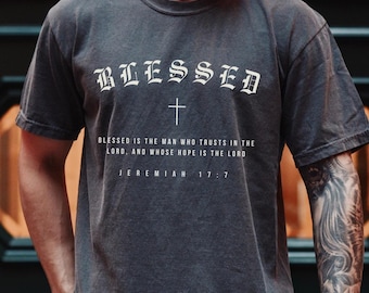 May include: Dark gray t-shirt with the word "BLESSED" in white gothic lettering above a cross. Below the cross is the text "BLESSED IS THE MAN WHO TRUSTS IN THE LORD, AND WHOSE HOPE IS THE LORD. JEREMIAH 17:7."