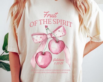 May include: A cream coloured t-shirt with a pink cherry graphic and the text "Fruit of the Spirit" and "Galatians 5:22-23". The text below the graphic reads "Love, Joy, Peace, Patience, Kindness, Goodness, Faithfulness, Gentleness, Self-Control."