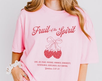 May include: Pink t-shirt with a graphic of two strawberries with a bow and the text "Fruit of the Spirit" and a Bible verse. The text reads "Love, Joy, Peace, Patience, Kindness, Generosity, Faithfulness, Gentleness, Self-Control Galatians 5:22-23"