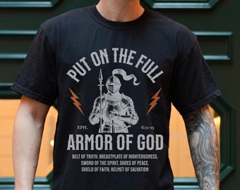 Op de afbeelding: Zwart T-shirt met een witte afbeelding van een ridder in harnas. De afbeelding bevat de tekst "Put on the Full Armor of God" en de Bijbeltekst "Eph. 6:11-13".