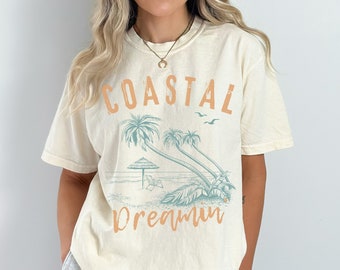 May include: A cream colored t-shirt with a graphic print of palm trees and the text "Coastal Dreamin".