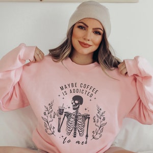 May include: Pink sweatshirt with a skeleton holding a coffee cup and the text "Maybe coffee is addicted to me".