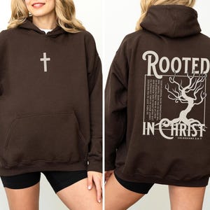 May include: A brown hoodie with a cross on the front and the text "Rooted in Christ" and a tree graphic on the back. The text also includes "Colossians 2:6-7".