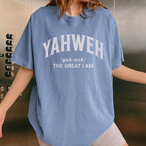 Op de afbeelding: Een lichtblauw T-shirt met de tekst "YAHWEH / yah-weh/ THE GREAT I AM" in wit gedrukt.