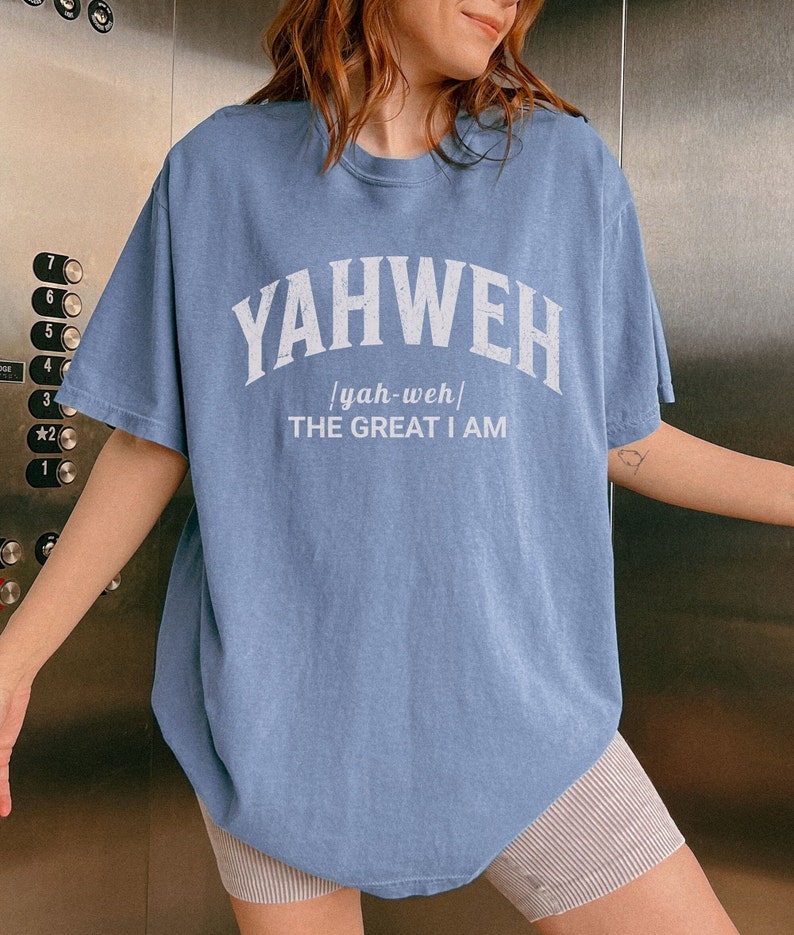Op de afbeelding: Een lichtblauw T-shirt met de tekst "YAHWEH / yah-weh/ THE GREAT I AM" in wit gedrukt.