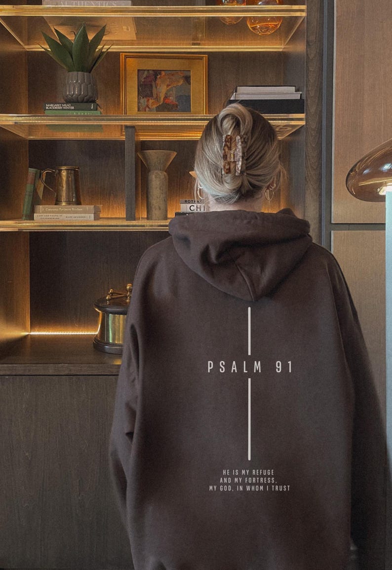 May include: A brown hoodie with the text "PSALM 91" and a vertical line design. Below the text is the quote "HE IS MY REFUGE AND MY FORTRESS, MY GOD, IN WHOM I TRUST" in white. The hoodie is worn by a person.