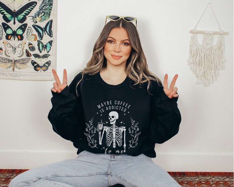 May include: Black sweatshirt with a white skeleton holding a coffee cup and the text "Maybe coffee is addicted to me".