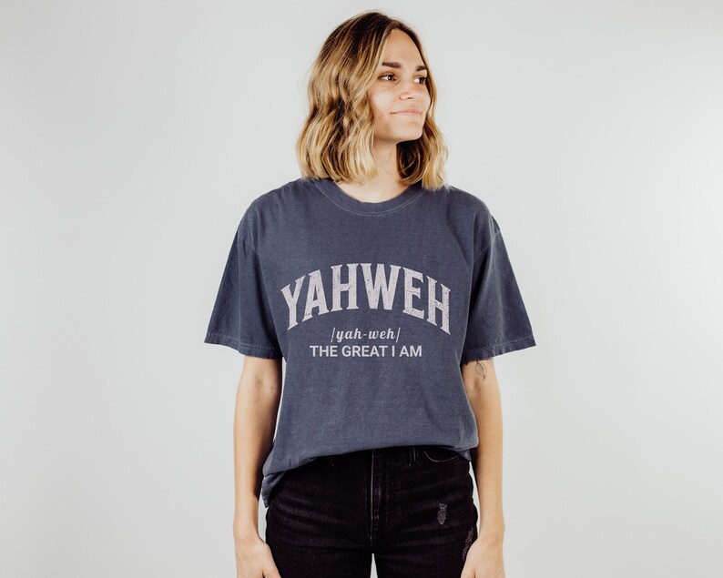 Op de afbeelding: Een donkerblauw T-shirt met witte tekst die "YAHWEH [yah-weh] THE GREAT I AM" zegt.