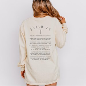 Może przedstawiać: Długi rękawowy t-shirt w kolorze kremowym z nadrukiem "PSALM 23" i krzyżem na plecach. Tekst zawiera werset z Biblii, Psalm 23.