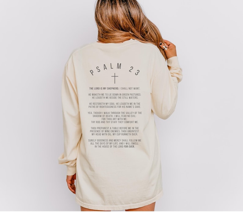 Może przedstawiać: Długi rękawowy t-shirt w kolorze kremowym z nadrukiem "PSALM 23" i krzyżem na plecach. Tekst zawiera werset z Biblii, Psalm 23.