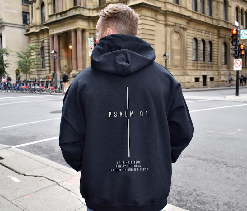May include: Black hooded sweatshirt with the text "PSALM 91" and a vertical cross design on the back. Below the text is the phrase "HE IS MY REFUGE AND MY FORTRESS, MY GOD, IN WHOM I TRUST" in white.