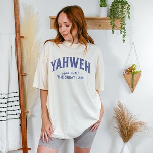 Op de afbeelding: Een cr&egrave;mekleurig T-shirt met een blauwe afbeelding waarop "YAHWEH /yah-weh/ THE GREAT I AM" staat.